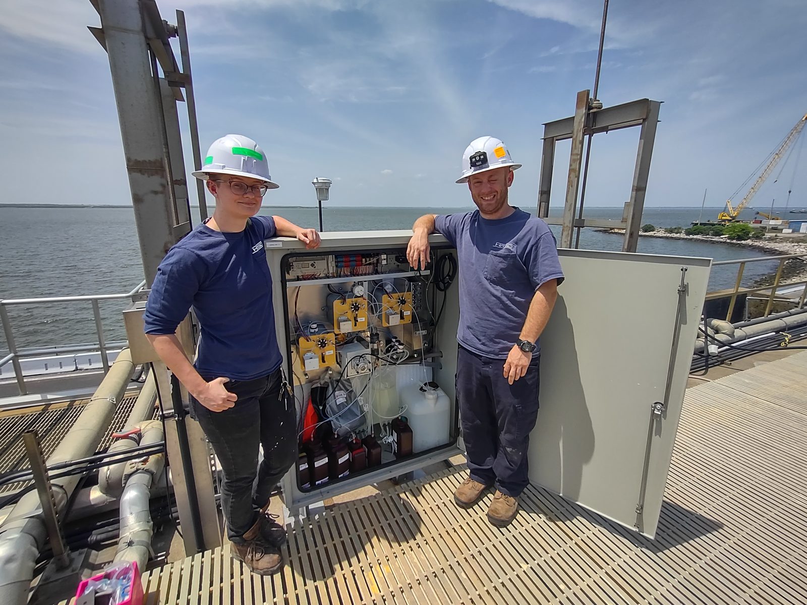 Two HRSD operators standing with an open Jarbalyzer cabinet on a waterside platform